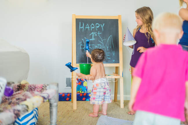 Toddler playing with balloon at blackboard at birthday party — Stock Photo