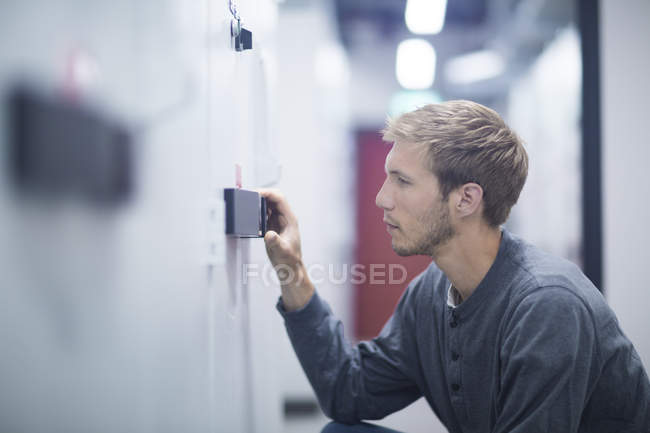 Male technician crouching to turn switch in technical room — Stock Photo