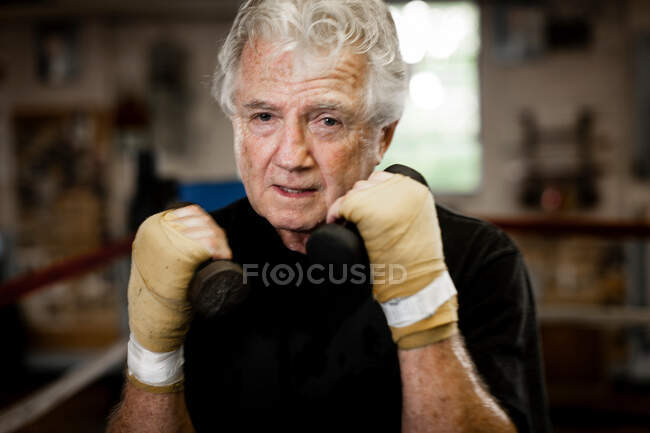 Старший чоловік носить рукавички, піднімаючи ваги — стокове фото