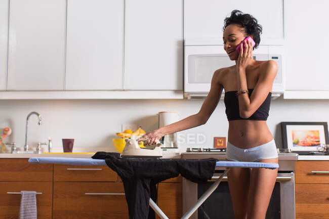 Young woman on cell phone ironing in underwear — Stock Photo