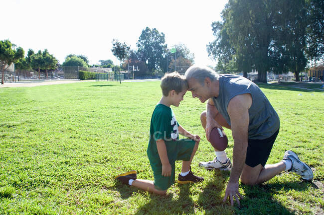 Boy and grandfather head to head, man holding football — Stock Photo