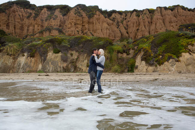 Зрелая пара, стоящая в море и целующаяся — стоковое фото