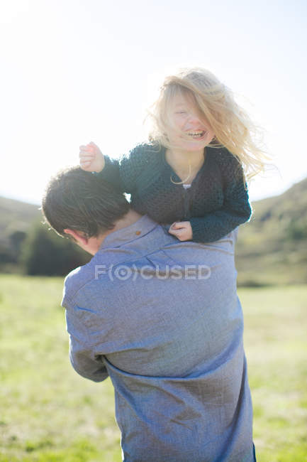 Portrait of girl being carried over father's shoulder in field — Stock Photo