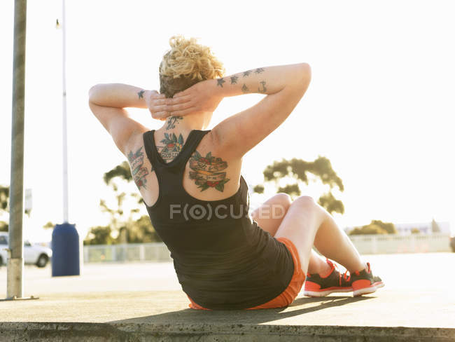 Rear view of young woman doing sit ups in parking lot — Stock Photo