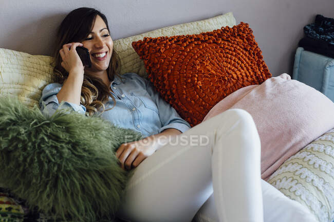 Young woman reclining on shabby chic bed making smartphone call — Stock Photo
