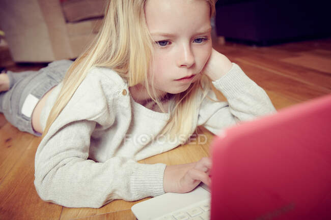 Une jeune fille couchée sur le sol avec un ordinateur portable — Photo de stock