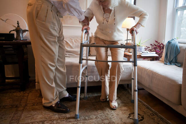 Senior man assisting wife with walking frame at home — Stock Photo