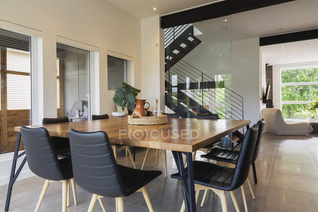 Mesa de jantar de madeira de noz americana e cadeiras de couro preto com pernas de madeira de cinzas na sala de jantar dentro de uma moderna casa de estilo cubo, Quebec, Canadá — Fotografia de Stock