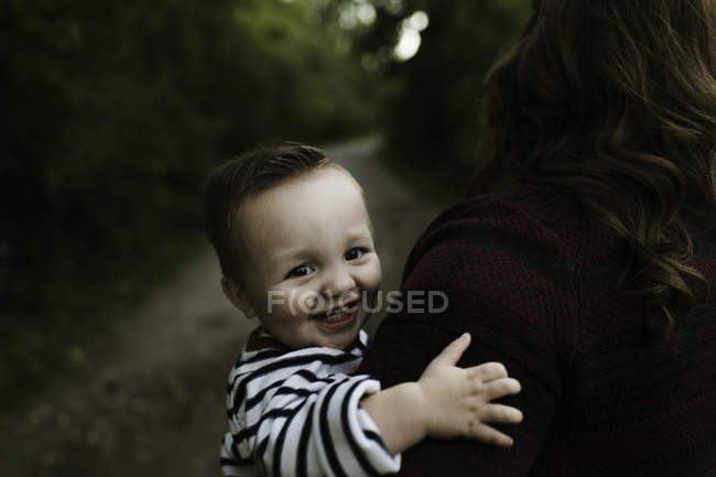 Bébé garçon dans les bras de la mère regardant la caméra sourire — Photo de stock