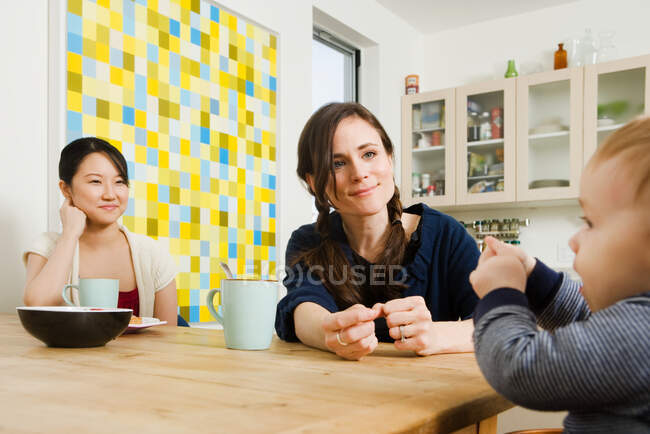 Amigos e um menino sentados em uma cozinha — Fotografia de Stock
