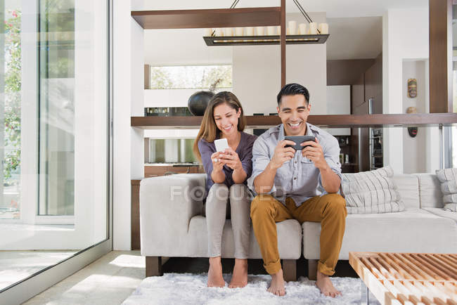 Paar spielt auf dem Sofa im Wohnzimmer Spiele auf Smartphones — Stockfoto