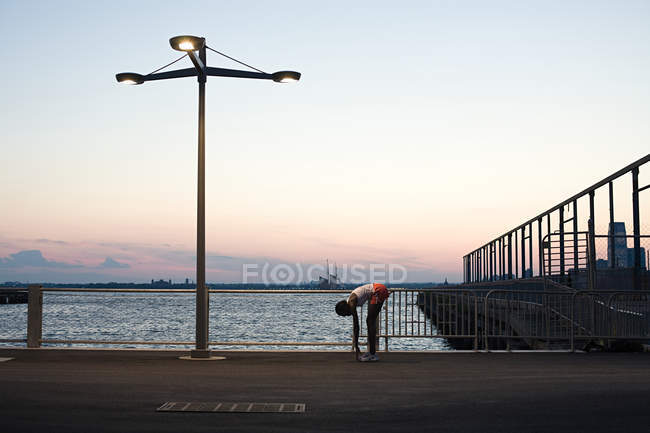 Runner stretching by river — Stock Photo
