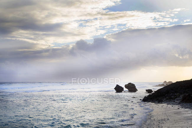 Rocks on coastline and ocean with sunlight in sky — Stock Photo