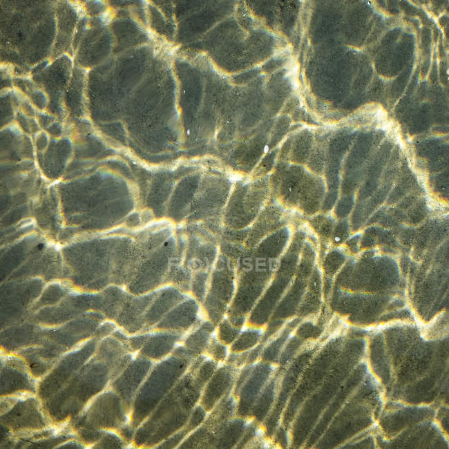 Meerwasser bricht Sonnenstrahlen auf sandigem Grund — Stockfoto