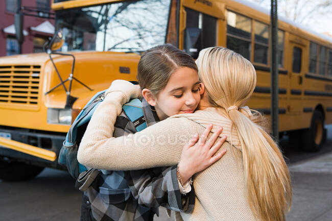 Menina e mãe abraçando de ônibus escolar — Fotografia de Stock