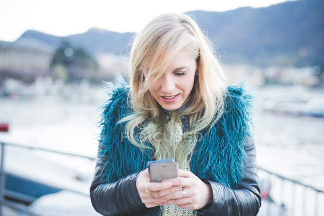 Mujer joven usando smartphone por lago - foto de stock