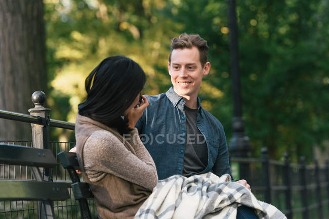 Mediados de la mujer adulta sentado en el banco del parque fotografiando novio en la cámara SLR - foto de stock