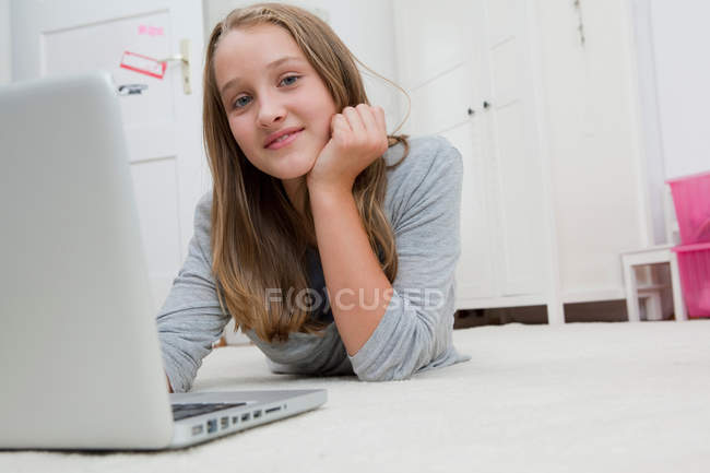 Усміхнена дівчина використовує ноутбук на підлозі, фокус на передньому плані — стокове фото