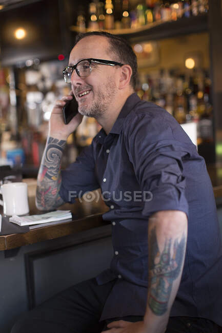 Barman hablando por teléfono inteligente en el mostrador de la casa pública - foto de stock