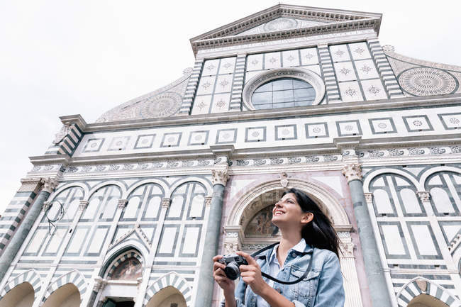 Visão de baixo ângulo da jovem mulher usando câmera digital na frente da igreja olhando para cima, Piazza Santa Maria Novella, Florença, Toscana, Itália — Fotografia de Stock