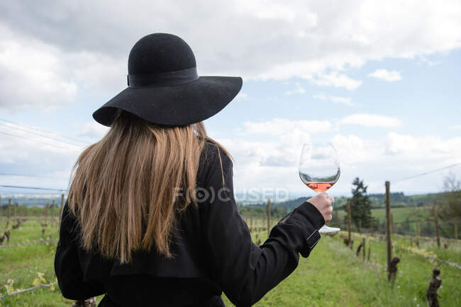 Woman standing in vineyard, holding glass of wine, rear view — Stock Photo