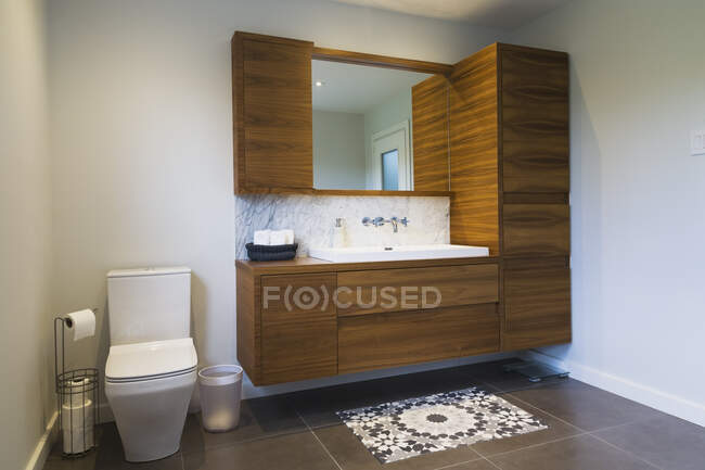 White high-back flush toilet and American walnut wood vanity with rectangular sink and ceramic tile flooring, Quebec, Canada — Stock Photo