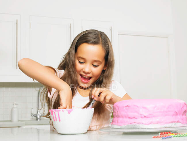 Girl (8-10) dipping finger in icing bowl — Stock Photo