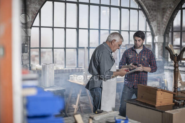 Ciudad del Cabo, Sudáfrica, anciano artesano en taller intercambiando detalles desde su teléfono - foto de stock