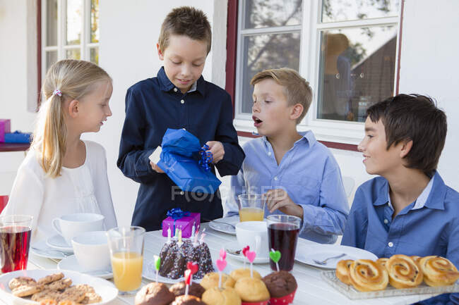 Junge mit Geschwistern packt Geburtstagsgeschenke auf Terrasse aus — Stockfoto