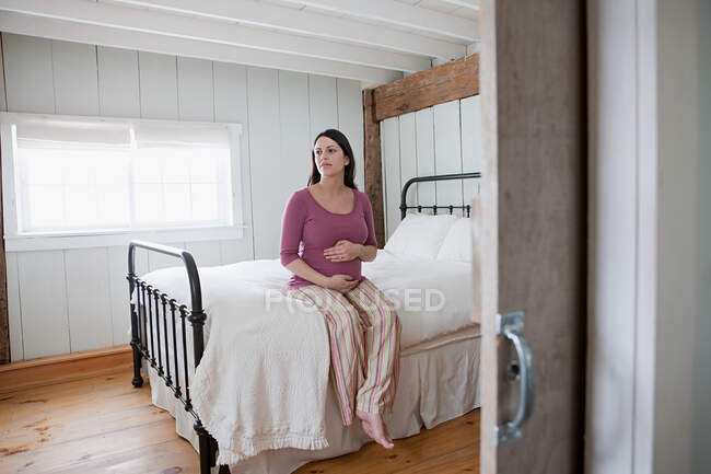Expectant mother sitting on bed — Stock Photo