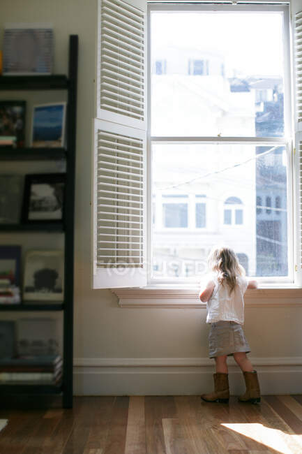 Rückansicht einer Kleinkindfrau, die durch das Wohnungsfenster blickt — Stockfoto