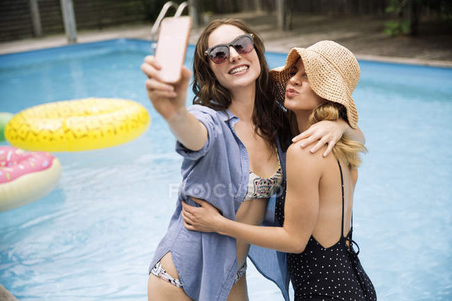 Women taking selfie with mobile phone beside swimming pool, Amagansett, New York, USA — Stock Photo