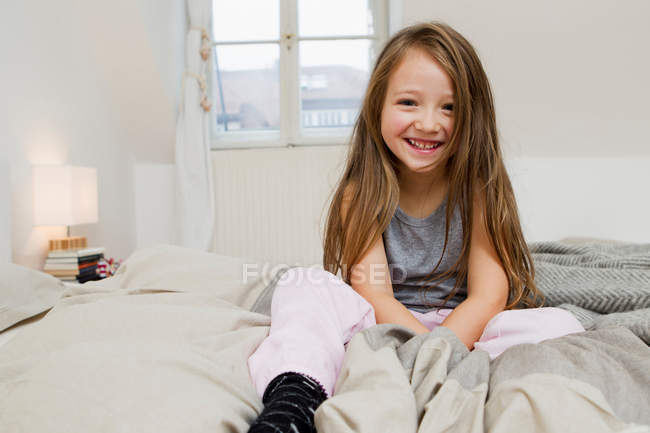 Smiling girl sitting on bed, focus on foreground — Stock Photo