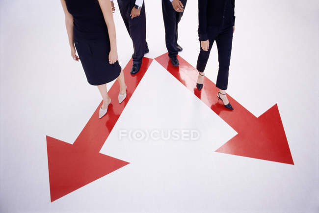 Four people walking along arrow signs — Stock Photo