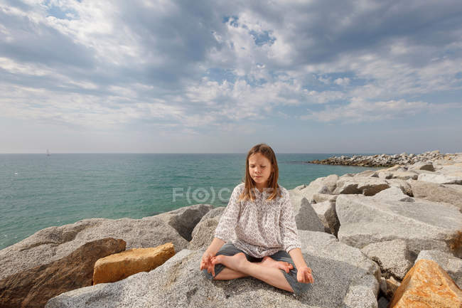 Ragazza meditando su rocce in spiaggia — Foto stock
