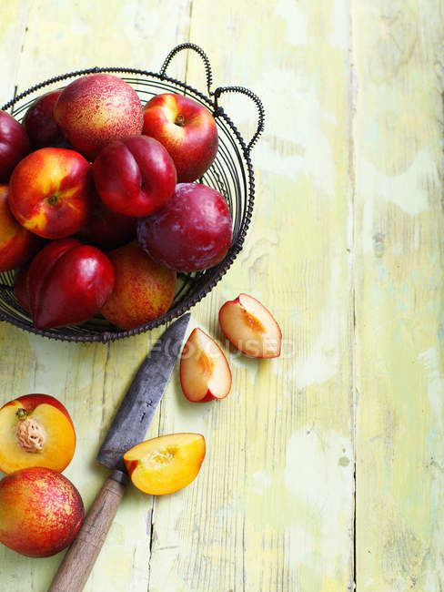 Prugne affettate su tavola di legno e frutta intera in cesto — Foto stock