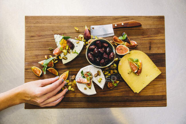 Placa de queso de variedad con higos, aceitunas, pistachos, cuchilla en tabla de cortar de madera - foto de stock