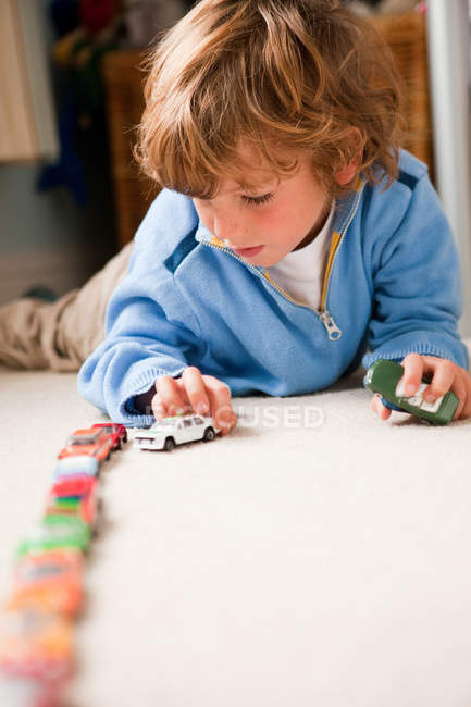 Young boy lining up toy cars in his bedroom — Stock Photo