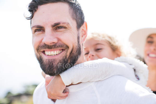 Chica teniendo cerdito espalda de padre en costa - foto de stock