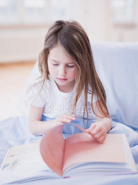 Молода дівчинка сидить у книжці з читання в ліжку. — стокове фото