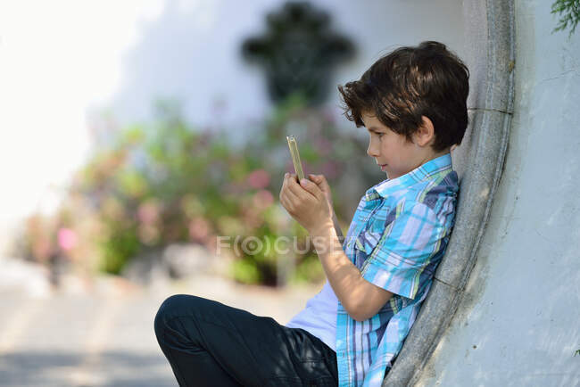 Niño apoyado contra la pared curvada mensajes de texto en el teléfono celular - foto de stock