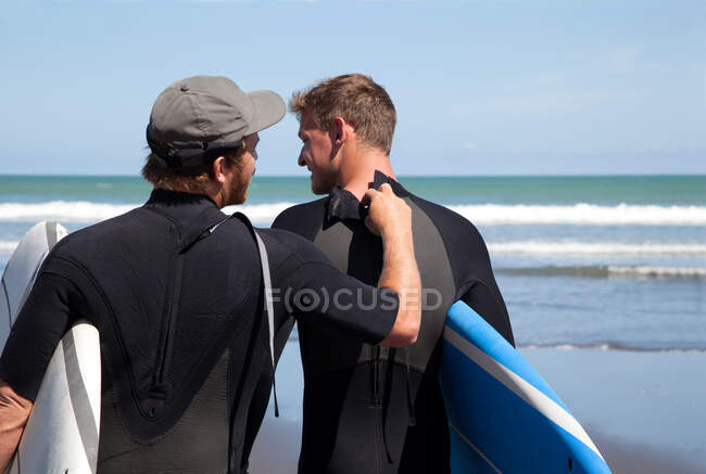 Vista trasera del surfista masculino revisando su cremallera de traje mojado amigos - foto de stock