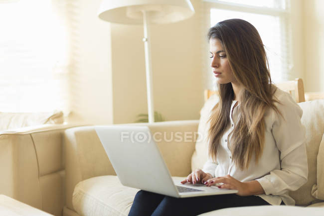 Молодая женщина сидит на диване, используя ноутбук — стоковое фото
