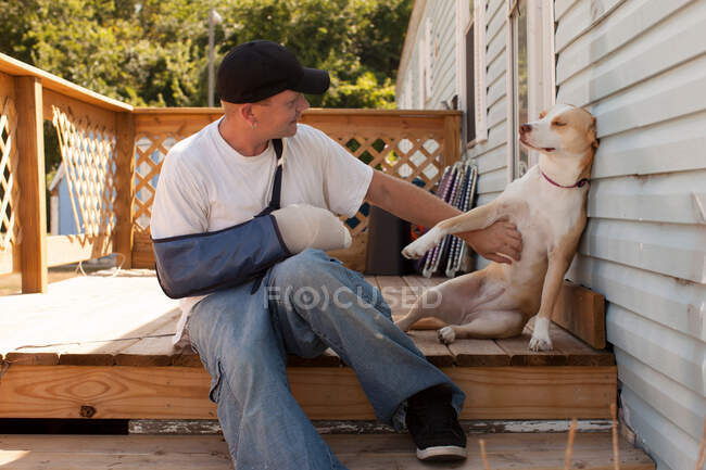 Man outside house with arm in sling and dog — Stock Photo