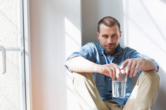 Hombre adulto medio sentado sosteniendo vaso de beber - foto de stock