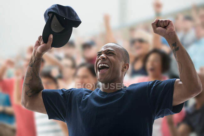 Hombre animando en el juego de deportes, sosteniendo la gorra de béisbol - foto de stock