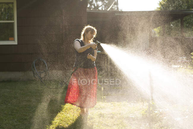 Frau besprüht Garten mit Wasser aus Gartenschlauch — Stockfoto