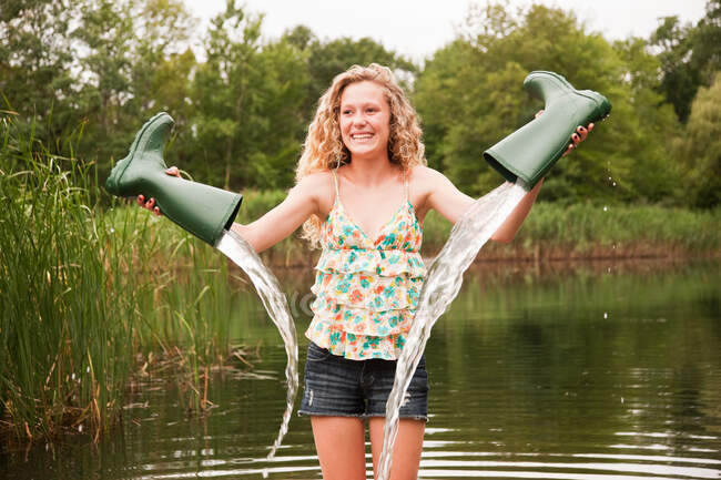 Teenage girl emptying wellies beside lake — Stock Photo