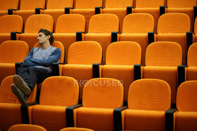 Joven somnoliento solo en el teatro de conferencias - foto de stock