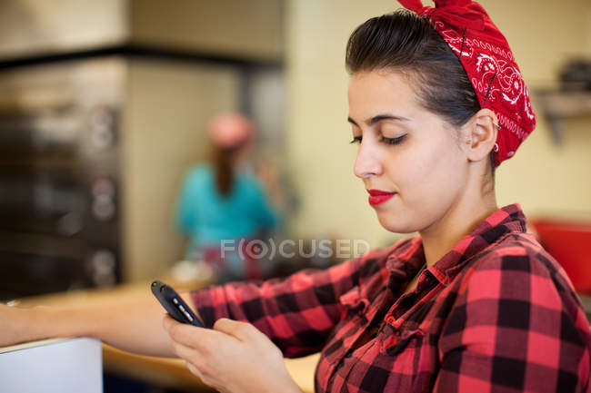 Молодая женщина использует мобильный телефон в пекарне — стоковое фото